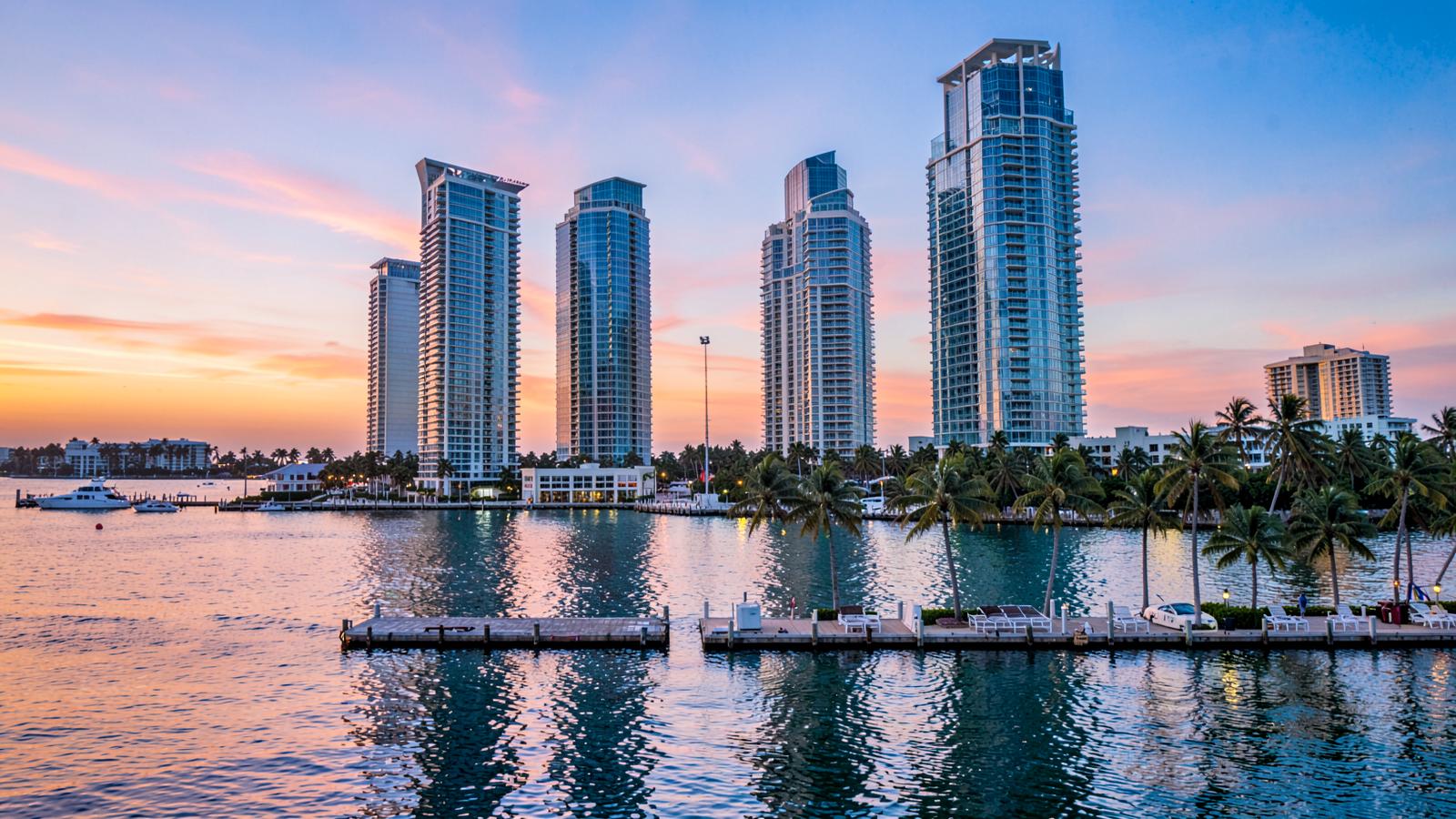 Torres modernas frente a la bahía de Miami al atardecer, con palmeras y agua en calma